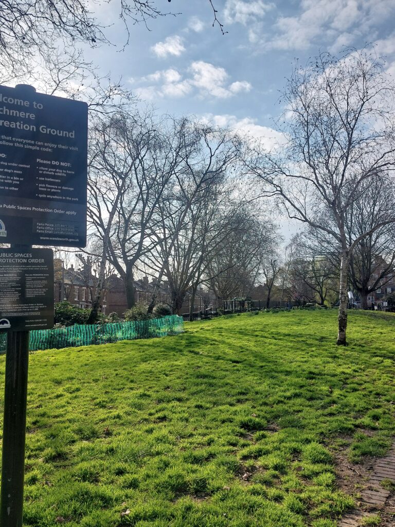 green site with the signs of the public space protection order on the left and trees